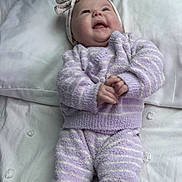 Peyton is registered to the contest to win money with this photo: baby, infant, newborn, headband, bow, pillow, bed, blanket, pajamas, striped_clothing, smiling, happy, chubby_cheeks, hands, portrait, lying_down, cozy, soft_texture, clothing, bedroom_background