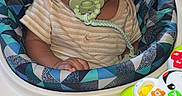 Jayquiell is registered to the contest to win money with this photo: baby, child, infant, sitting, pacifier, portrait, curly_hair, dark_skin, brown_eyes, looking_at_camera, activity_center, baby_toys, rattle, colorful, indoors, chair, patterned_fabric, emoji, smiling, close_up