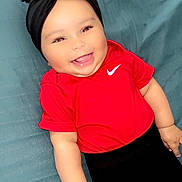 Keylissa a rejoint le concours — aidez-le/la à gagner de superbes lots ! apparel, baby, black_headband, cheeks, child, close_up, clothing, cute, eyes, face, hand, happy, indoor, infant, lying_down, person, portrait, red_shirt, skin, smiling