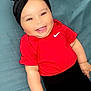 apparel, baby, black_headband, cheeks, child, close_up, clothing, cute, eyes, face, hand, happy, indoor, infant, lying_down, person, portrait, red_shirt, skin, smiling