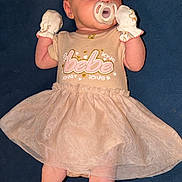 Bella joined the competition — help win amazing prizes! adorable, baby, bare_legs, blue_background, clothing_text, dress, face, feet, flash_lighting, head, infant, lying_down, mittens, newborn, onesie, pacifier, pacifier_in_mouth, pink_clothing, portrait, tutu