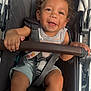 toddler, child, stroller, smiling, curly_hair, safety_harness, baby, happy, seat, clothing, outdoor, person, cute, infant, legs, hand, baby_stroller, seatbelt, playful, portrait