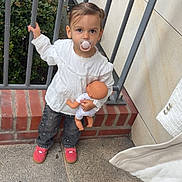 Kamilla a rejoint le concours — aidez-le/la à gagner de superbes lots ! toddler, child, pacifier, doll, white_blouse, jeans, red_shoes, metal_railings, brick_wall, concrete_floor, greenery, outdoor, person, baby_doll, holding, standing, casual_clothing, cute, young_child, portrait