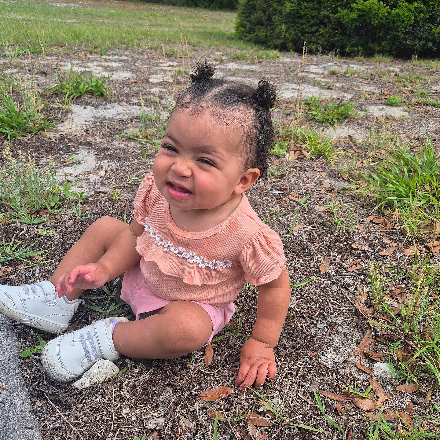 Sophia joined the competition — help win amazing prizes! toddler, child, sitting, outdoor, grass, dirt, shoes, curly_hair, pink_shorts, peach_top, nature, sunlight, cute, expression, summer, casual_clothing, small_person, greenery, daytime, young_kid