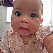 Sophia is registered to the contest to win money with this photo: baby, infant, face, eyes, pink_dress, clothing, indoor, portrait, child, curious, cute, expression, window, curtain, skin, person, young, head, sitting, closeup