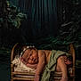 newborn, baby, sleeping, flower_crown, bed, blanket, green_cloth, infant, peaceful, portrait, wooden_bed, dark_background, forest_theme, cozy, cute, resting, soft_lighting, indoor, child, toddler