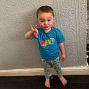 Leo joined the competition — help win amazing prizes! child, toddler, barefoot, blue_tshirt, patterned_pants, standing, wallpaper, dark_floor, indoor, playful, gesture, funny_face, person, young, cute, expression, home, floor, wall, casual_clothing