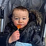 Leo joined the competition — help win amazing prizes! child, toddler, lollipop, stroller, jacket, blanket, fur_hood, hand, face, expression, outdoor, clothing, cold_weather, cute, person, blue_blanket, black_jacket, happy, baby, portrait