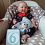 baby, black_pants, blanket, chair, child, clothing, cute, decor, heart_pattern, indoor, infant, milestone, person, plush_toy, portrait, red_bow_tie, sign, smiling, teddy_bear, text