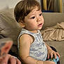 toddler, child, indoor, couch, toy, bracelet, sleeveless_shirt, animal_print, brown_hair, curious, seated, soft_lighting, home, casual, young_child, portrait, attention, small_hands, furniture, relaxed