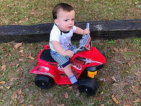Braedyn is registered to the contest to win money with this photo: baby, baby_toddler_clothing, carmine, child, grass, lawn, nose, person, plastic, play, red, riding_toy, tire_care, toddler, toy, toy_vehicle, tread, yard
