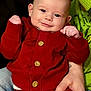 baby, infant, smile, face, blue_eyes, red_outfit, cardigan, wooden_buttons, hands, adult_hand, tattoo, green_sweater, jeans, portrait, indoor, couch, close_up, cute, soft_lighting, person