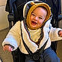 baby, child, smile, jacket, knit_hat, stroller, happy, infant, clothing, warm, cozy, indoor, person, cute, baby_face, young_child, seated, playful, protected, bundle