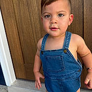 Noah Gabriel joined the competition — help win amazing prizes! toddler, child, denim_overalls, standing, door, wood, curious, face, skin, eyes, hair, outdoor, footwear_absent, expression, person, clothing, arm, hand, bracelet, young
