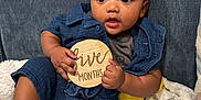 Kenneth is registered to the contest to win money with this photo: baby, baby_toys, blanket, blue_outfit, child, couch, curious, cute, five_months, happy, indoor, infant, milestone_sign, pacifier, portrait, relaxed, seated, smiling, socks, wooden_sign