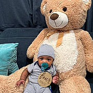 Kenneth joined the competition — help win amazing prizes! baby, teddy_bear, pacifier, striped_clothing, hat, plush_toy, couch, pillow, infant, child, indoors, cute, soft_toy, sitting, smiling, wooden_sign, four_months, blue_pillow, cozy, home