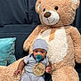 baby, teddy_bear, pacifier, striped_clothing, hat, plush_toy, couch, pillow, infant, child, indoors, cute, soft_toy, sitting, smiling, wooden_sign, four_months, blue_pillow, cozy, home