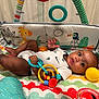 baby, infant, playpen, toy, colorful, animal_print, giraffe, bird, pattern, onesie, hand, foot, face, child, indoor, curious, plastic_toy, yellow_ball, blue_ring, playtime