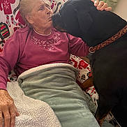 Winston joined the competition — help win amazing prizes! elderly_person, dog, blanket, couch, indoor, affection, love, pet, companion, cozy, comfort, hand, collar, red_sweater, curtains, patterned_blanket, home, interaction, face, animal