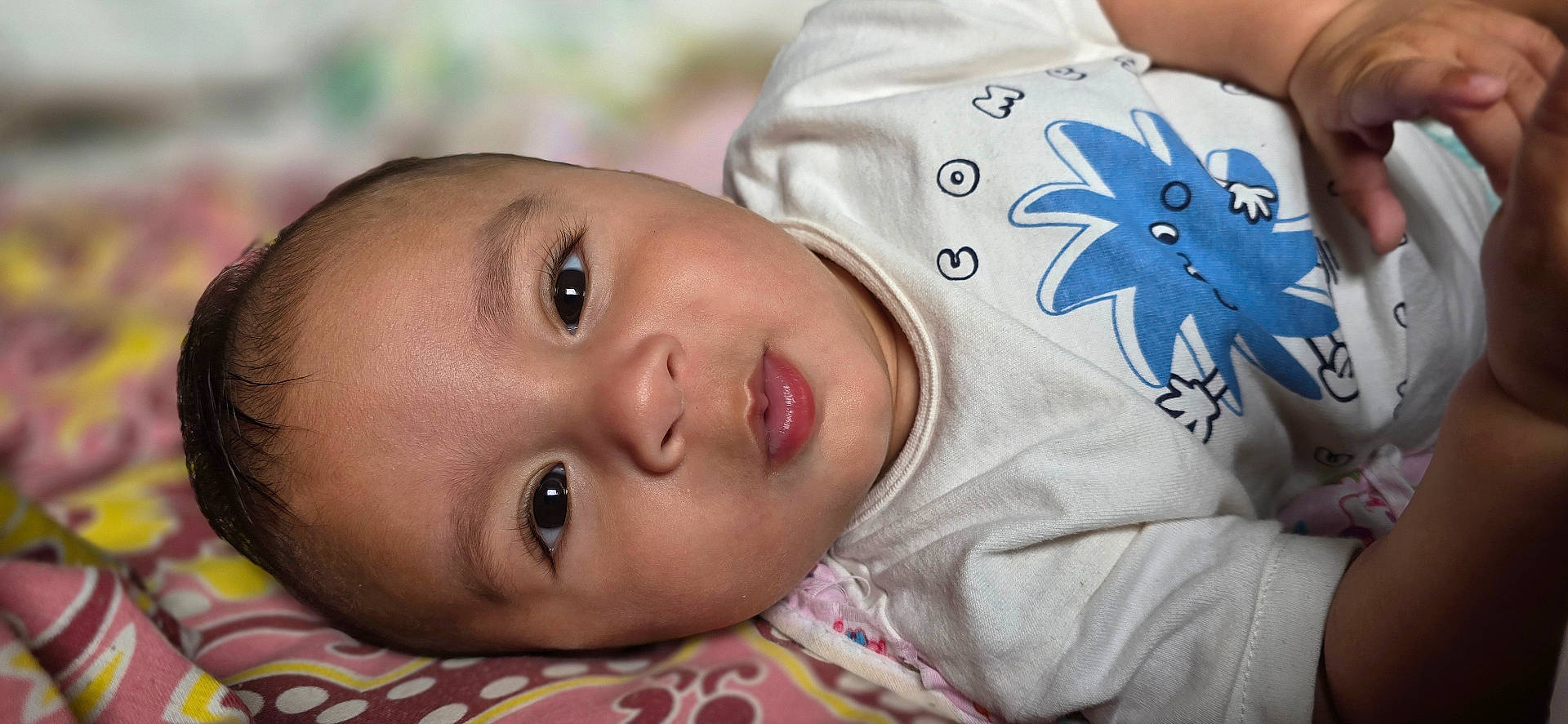 Qaelen joined the competition — help win amazing prizes! baby, blanket, blue_cartoon, child, closeup, comfortable, cute, expression, eyes, face, hand, indoors, infant, lying_down, pattern, portrait, shirt, skin, soft, young