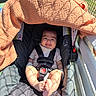 baby, car_seat, blanket, sunlight, shadow, smiling, infant, straps, outdoor, fence, feet, clothing, safety, child, seat, happy, person, daylight, relaxing, cute