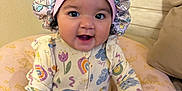 Genesis is registered to the contest to win money with this photo: baby, child, infant, smiling, bonnet, onesie, colorful_clothing, pink_cushion, princess, crown_pattern, indoor, seated, happy, cute, portrait, young_child, hand, face, headwear, cozy