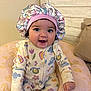 baby, child, infant, smiling, bonnet, onesie, colorful_clothing, pink_cushion, princess, crown_pattern, indoor, seated, happy, cute, portrait, young_child, hand, face, headwear, cozy