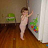 Daisy is registered to the contest to win money with this photo: toddler, child, pajamas, barefoot, wooden_floor, cabinet, toys, plastic_bag, high_chair, indoor, home, furniture, colorful, baby, person, standing, reaching, young_child, floor, playtime