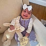 baby, bow, stuffed_animal, couch, wooden_sign, milestone, happy, smiling, purple_overalls, white_socks, infant, indoor, wood_floor, headband, child, soft_toy, person, cute, celebration, portrait