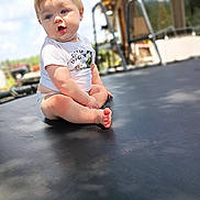 Kayson joined the competition — help win amazing prizes! baby, child, toddler, sitting, trampoline, outdoor, backyard, sunlight, blue_sky, portrait, face, eyes, smiling, surprised, white_shirt, shorts, barefoot, playground, wooden_house, photography