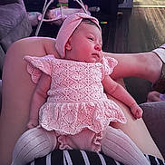 Rosalynn joined the competition — help win amazing prizes! baby, infant, pink_clothing, headband, knitted_outfit, person, lap, living_room, furniture, television, baby_swing, flooring, striped_clothing, relaxed, indoor, couch, wood_floor, toy, comfort, home