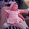 baby, infant, pink_clothing, headband, knitted_outfit, person, lap, living_room, furniture, television, baby_swing, flooring, striped_clothing, relaxed, indoor, couch, wood_floor, toy, comfort, home