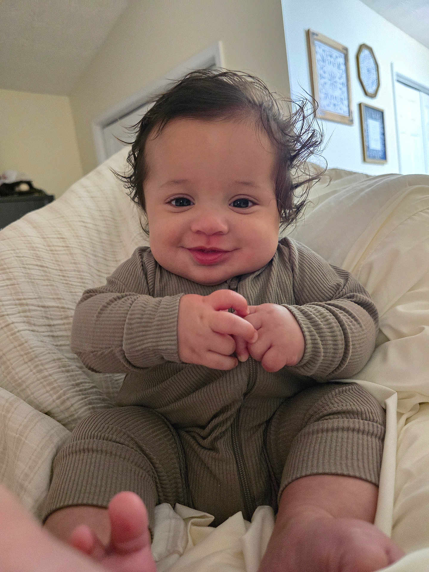 Myles is registered to the contest to win money with this photo: baby, infant, smiling, clothing, hands, face, hair, bed, blanket, indoors, person, cute, happy, onesie, foot, skin, portrait, child, room, wall_art
