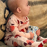 Karter Jane is registered to the contest to win money with this photo: baby, child, pajamas, fruit_pattern, phone, handheld_device, couch, textile, patterned_clothing, footed_pajamas, infant, side_profile, expression, indoors, soft_lighting, seated, cute, small_hands, cozy, home