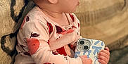 Karter Jane is registered to the contest to win money with this photo: baby, child, couch, cozy, cute, expression, footed_pajamas, fruit_pattern, handheld_device, home, indoors, infant, pajamas, patterned_clothing, phone, seated, side_profile, small_hands, soft_lighting, textile