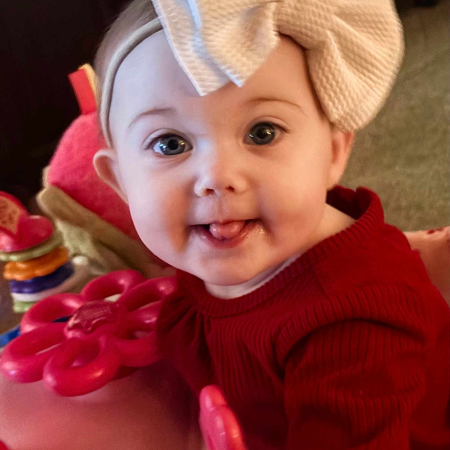 Karter Jane is registered to the contest to win money with this photo: baby, bow, child, closeup, colorful, cute, expression, face, happy, headband, indoor, infant, person, playful, red_sweater, smile, soft_lighting, toddler, tongue, toy