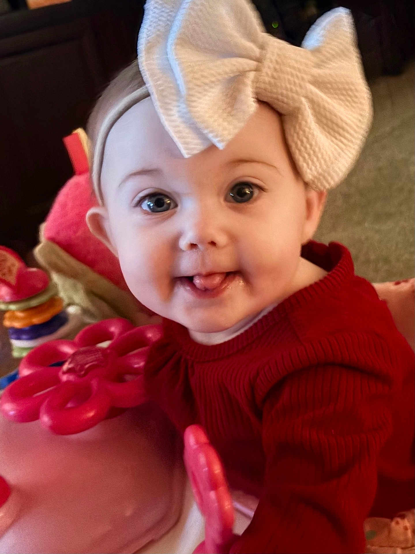 Karter Jane is registered to the contest to win money with this photo: baby, child, toddler, face, bow, headband, red_sweater, toy, indoor, playful, cute, expression, tongue, closeup, person, infant, colorful, soft_lighting, happy, smile