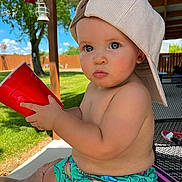 Micah is registered to the contest to win money with this photo: toddler, child, blue_eyes, hat, cap, red_cup, shorts, dinosaur_print, outdoor, backyard, grass, fence, patio, hand, sunny, summer, cute, baby, portrait, sitting