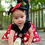 baby, child, crawling, red_dress, polka_dots, headband, minnie_mouse, costume, outdoor, wooden_deck, hand, face, expression, curious, cute, person, nature, greenery, soft_focus, playful