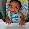 toddler, child, smiling, high_chair, baby, curly_hair, blue_shirt, seatbelt, indoor, person, cute, happy, hands, face, portrait, feeding, colorful, patterned_background, baby_gear, infant