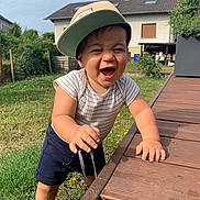 Marius participe au concours pour gagner de l'argent avec cette photo : toddler, child, smiling, cap, striped_shirt, shorts, barefoot, wooden_deck, grass, flowers, garden, house, outdoor, daylight, happy, person, young_child, playful, summer, nature