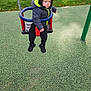 Boston is registered to the contest to win money with this photo: toddler, child, swing, playground, jacket, beanie, outdoor, fence, grass, safety_surface, chain, red, blue, black_shoes, cold_weather, park, person, daytime, serious_expression, playing