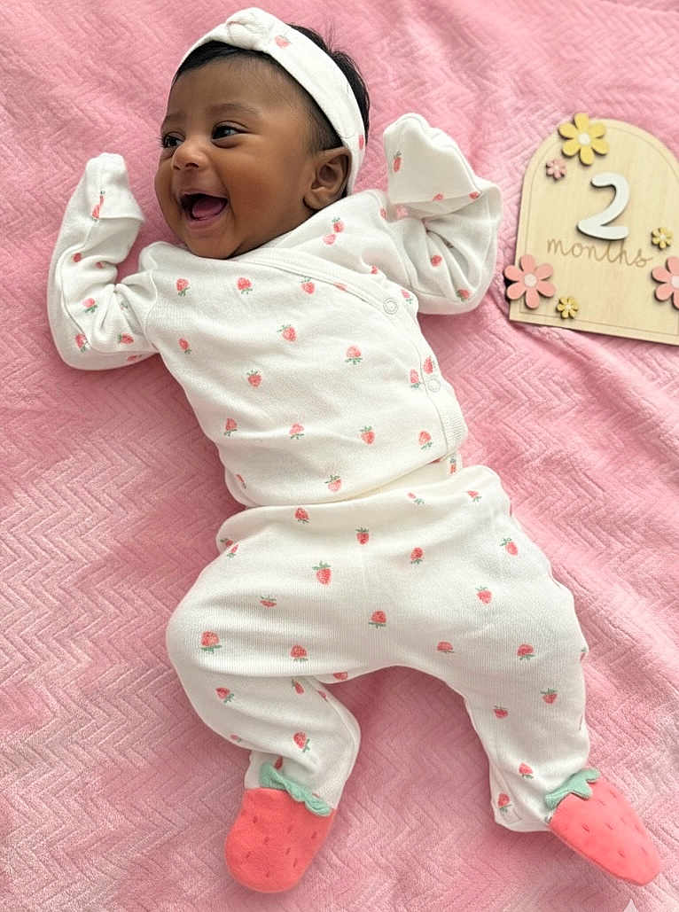 Evangeline is registered to the contest to win money with this photo: baby, infant, smiling, happy, white_clothing, headband, pink_blanket, strawberry_pattern, cute, newborn, milestone_sign, wooden_sign, flower_decor, lying_down, child, footwear, soft_texture, portrait, indoors, celebration