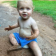 Josiah is registered to the contest to win money with this photo: toddler, child, dirt, mud, blue_shorts, bare_chest, outdoor, grass, gravel_path, play, happy, messy, nature, barefoot, summer, expression, sitting, daylight, cute, curly_hair