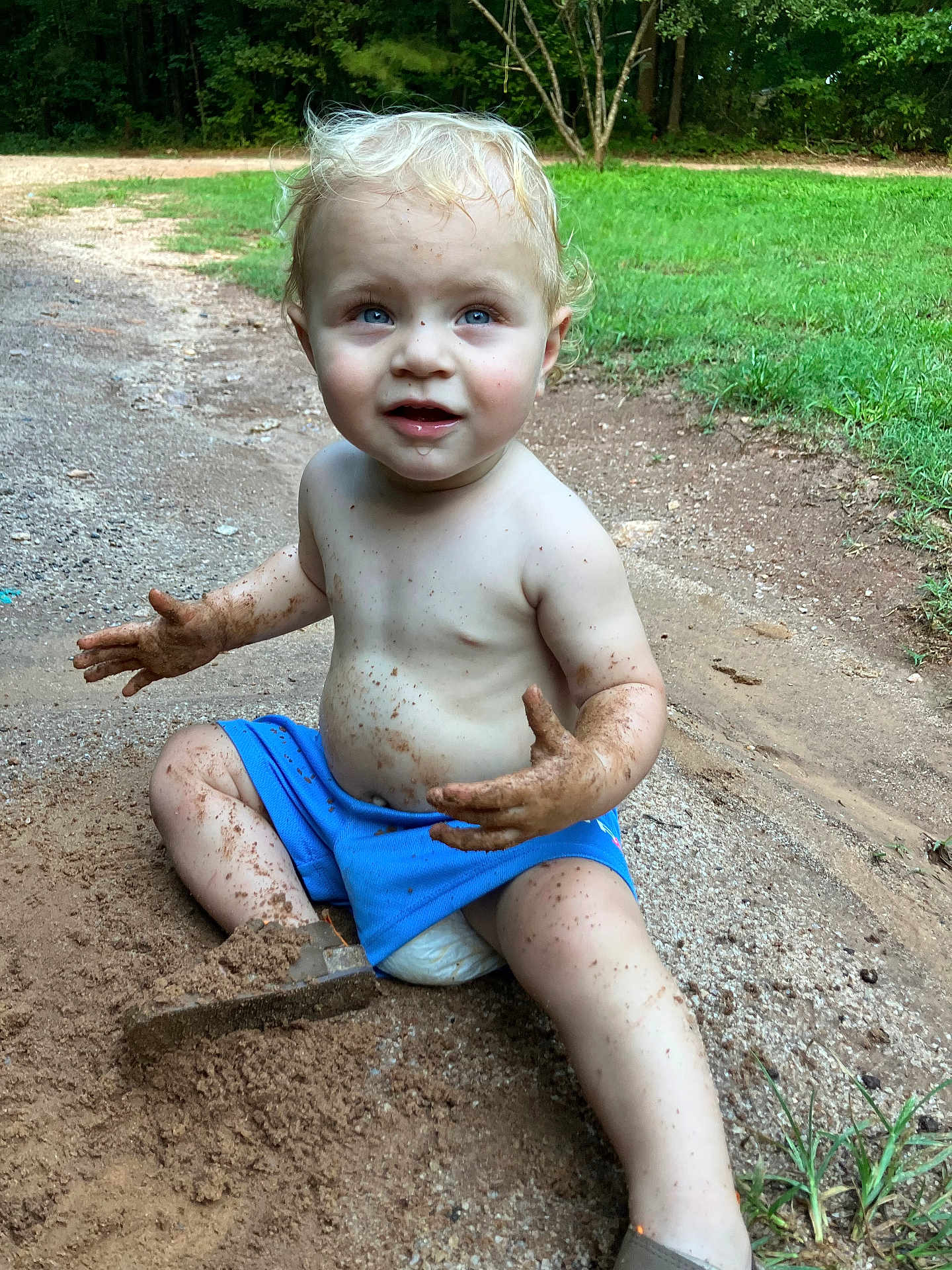 Josiah is registered to the contest to win money with this photo: toddler, child, dirt, mud, blue_shorts, bare_chest, outdoor, grass, gravel_path, play, happy, messy, nature, barefoot, summer, expression, sitting, daylight, cute, curly_hair