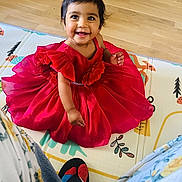 Kiara participe au concours pour gagner de l'argent avec cette photo : child, toddler, red_dress, smiling, sitting, play_mat, floor, wood_floor, indoor, person, happy, cute, baby, clothing, footwear, home, colorful, portrait, bright, young