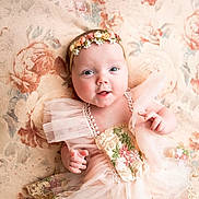 Charlie is registered to the contest to win money with this photo: baby, infant, flower_crown, dress, floral, blanket, smile, cute, portrait, child, happy, soft_lighting, indoors, tulle, headband, hands, skin, closeup, laying_down, adorable