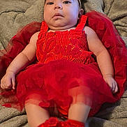 Esmeralda is registered to the contest to win money with this photo: baby, infant, red_dress, headband, bow, blanket, soft_texture, cute, heart_pattern, footwear, lying_down, portrait, closeup, indoors, child, adorable, fuzzy, warm, expression, person