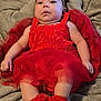baby, infant, red_dress, headband, bow, blanket, soft_texture, cute, heart_pattern, footwear, lying_down, portrait, closeup, indoors, child, adorable, fuzzy, warm, expression, person