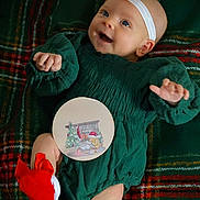 Layla joined the competition — help win amazing prizes! baby, infant, smiling, green_dress, red_bow, red_socks, headband, plaid_blanket, holiday, christmas_theme, cute, happy, child, portrait, indoors, cozy, laying_down, festive, person, celebration